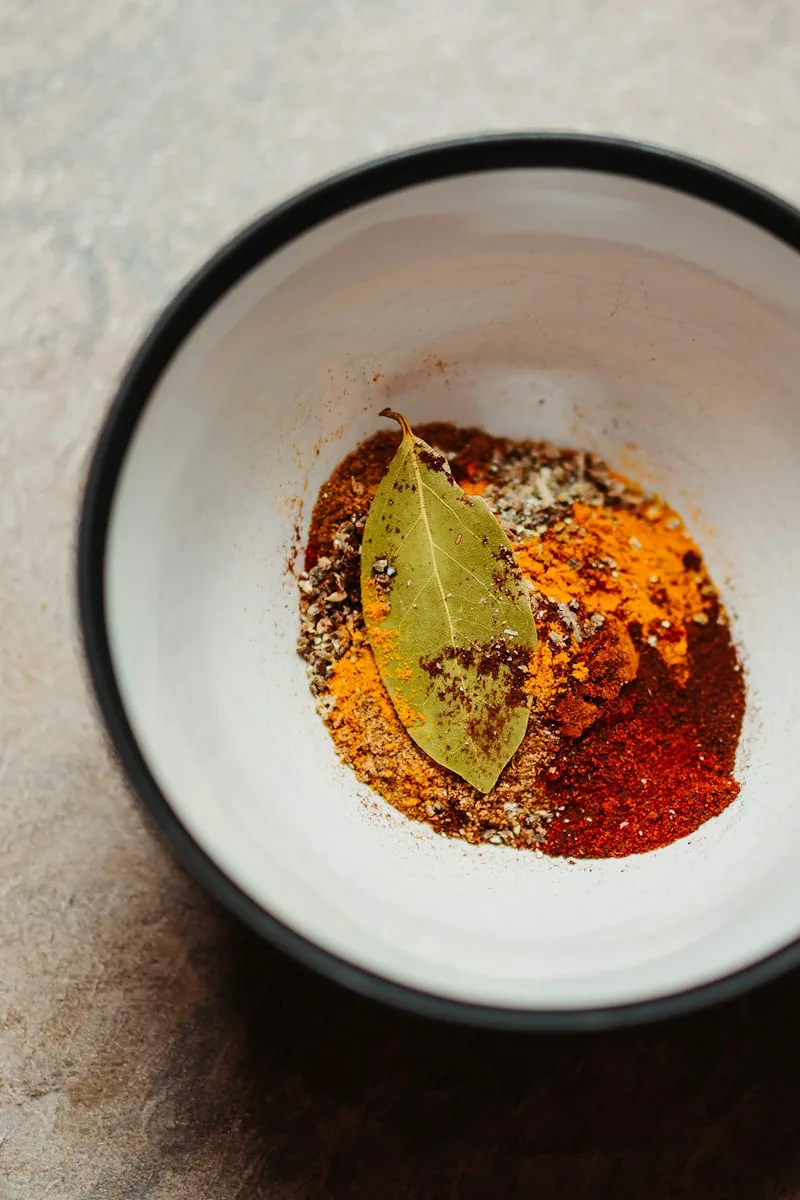 White bowl with ground spices and a bay leaf